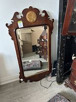 Full view of the large decorative mirror leaning against a wall, showing the marbled wood frame and overall condition.