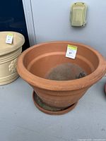Front angle view of large terra-cotta pot with base and dirt inside, showing rim and body shape.