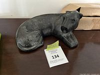 Front and side view of dark marble jaguar/leopard sculpture on dark surface with label number 134.