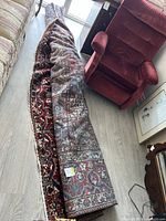 Partially rolled wool rug laid on floor next to armchair, showing overall size and backing