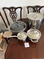 Full view of four cookware pieces on table including large stock pot, sauté pan, small saucepan, and additional pan, all with lids.