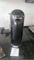 Front view of black Nespresso Vertuo Plus coffee maker, showing the coffee outlet and drip tray.