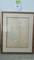 Framed pencil sketch of nude figure showing full figure, arms raised, initialed with visible mat and wood frame.