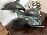 Side angle showing the two dolphins in mid-leap with green patina and black base.