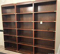 Three large wooden bookshelves with multiple shelves each and gold-tone metal accents on corners and edges. Shelves are dark wood color and arranged side by side.