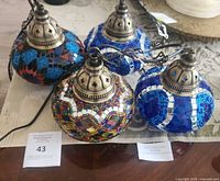 Four Turkish mosaic pendant lamps grouped together on a table showing varied colorful glass tile patterns and metal tops.