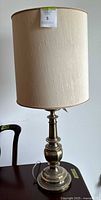Full view of vintage brass table lamp with beige/cream textured fabric lampshade on a table.