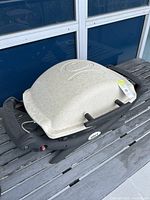 Top and side view of the beige/off-white portable Weber gas grill with black handles and base, showing light residue on the grill surface and Weber brand logo.