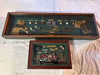 Long rectangular shadow box showing miniature woodworking tools with paper labels on green felt background.