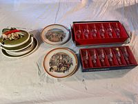 Wide view of entire lot showing two sets of crystal glasses in labeled boxes, two collector plates with horse racing themes, and ceramic soup tureen with vegetable motif on lid.