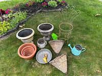Assorted gardening pots, planters, watering cans, and garden tools arranged on grass near garden bed.