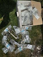 Multiple packaged metal cabinet handles and knobs in a box, assorted styles but predominantly tubular metal handles and knobs, silver finish.