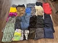 Photo of assorted ladies pants, skirts, and shorts arranged on floor showing variety of colors and styles including denim, prints, and solids.