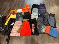 Full view of the assorted ladies clothing items laid out on a wood floor including skirts, pants, and shorts in various colors and patterns.