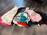 Photo of assorted ladies tank tops and tees laid out on the floor. Colors include white, pink, teal, black, red, gray, and maroon. Mix of short sleeve and sleeveless casual tops.