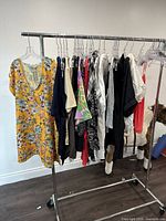 Wide view of assortment of 14 ladies' tops hanging on a clothing rack, showing variety in colors and patterns.