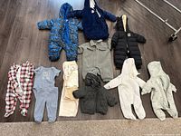 Overview of assorted baby outerwear and clothing including various snowsuits, rompers, sleepwear, and small towels.