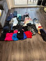 Full view of assorted pants, skirts, and shorts laid out on the floor mostly in dark, bright, and pastel colors with visible tags.
