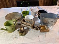 Wide view showing assorted planters, watering can, wooden wheelbarrow, and garden figurines arranged on a table.