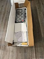 Open box showing unassembled components of white and black bar shelf including panels and hardware.