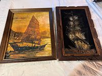 Two framed ship artworks shown side by side on a white fabric surface.
