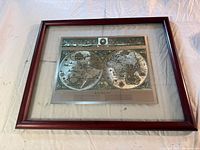 Wide view of the framed artwork displaying the Blaeu world map (two hemispheres) inside a reddish wood frame with glass.