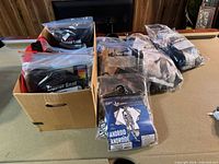 Box containing multiple sealed Halloween kids costumes in plastic bags, some packaging visible.