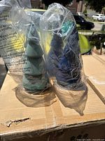 Two mini Christmas trees individually wrapped in clear plastic bags on a cardboard surface, showing the tree colors and shape.