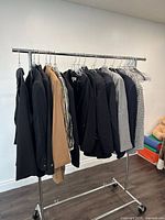 Photo of a rack holding multiple ladies blazers in assorted colors and patterns, mainly black, beige, grey, and checked patterns.