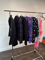 Front side view of assorted ladies blazers and jackets on a clothing rack, showing variety of colors and patterns including solid black, plaid, floral, polka dots, and pinks.