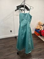 Front view of ladies size 8 teal satin gown on hanger against white wall and dark floor, showing fitted bodice and flared skirt.