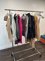 Photo showing eight assorted ladies jackets hanging on metal rack, colors include beige, blue denim, pink, grey, black, and beige faux fur.