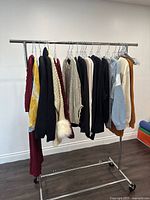 Rack of assorted ladies sweaters including knit, fleece, and sweatshirt styles in multiple colors such as dark red, cream, black, light blue, and brown tones.