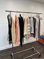 Photo showing 9 assorted women's medium sweaters on a metal rolling clothing rack against a wall with hardwood floor.