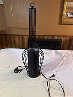Photo showing a black metal cage table lamp with a cylindrical inner shade and attached power cord