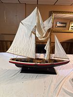 Full view of the model ship from the side showing its white sails, black and red hull, and mounted display stand.