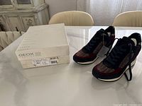 Geox sneaker pair and original shoe box shown on a table with neutral background.