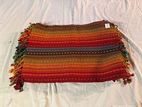 Single colorful woven placemat showing multicolored horizontal stripes and tassel fringes on edges.