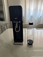 Black Sodastream soda maker and one reusable bottle on table