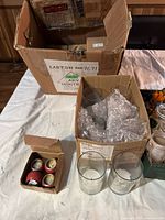 Large cardboard box containing many small boxes of candles, wrapped in bubble wrap, also visible are some loose glass candle holders in another box