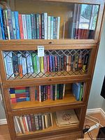 Full view of three shelves in a wooden bookcase filled with assorted books including fiction, cookbooks, and children's literature.