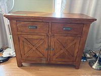 Wood buffet front view showing two drawers and two cabinet doors with X-pattern design and metal hardware.