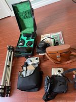 Overview of all items showing Pentax 35mm camera in green lined case, HP Photosmart 318 camera with tripod, Slik Gazelle 95D tripod, binoculars, HP Photosmart M527 camera, various camera cases and accessories.