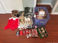 Overview of all Christmas decorations including stockings, ornaments, figurines, and storage bin on a hardwood floor.