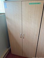 Front view of a wooden two-door cupboard, closed, showing light wood grain finish and silver handles.