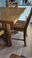 Side angle view of the wooden dining table and one chair showing table surface and part of chair seat and legs