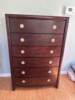 Front view of six-drawer wooden dresser in dark stain with silver round drawer pulls.