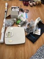 Overview of all items showing spin scrubber with attachments, Renpho massager with bag and charger cables, and digital scale on wood floor.