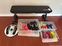 Photo showing black Max Pro exercise bench with plastic containers of various hand weights and the white Revitive Circulation Booster unit placed on floor nearby.
