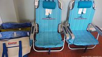 Two turquoise blue Tommy Bahama folding chairs with reusable shopping bags beside them.